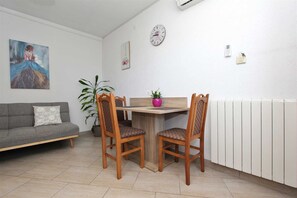 Ein Essbereich mit Holztisch und -stühlen, einer Uhr, einem Heizkörper, einer Couch und einem Gemälde an der Wand.