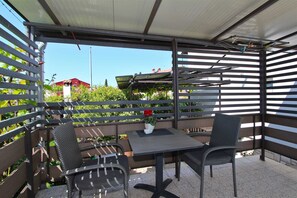 Eine Terrrasse im Freien mit Tisch und zwei Stühlen, einem Blumentopf und Blick auf Gebäude und Grünflächen.