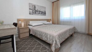 Een slaapkamer met een bed, nachtkastje, bureau en raam met gordijnen.
