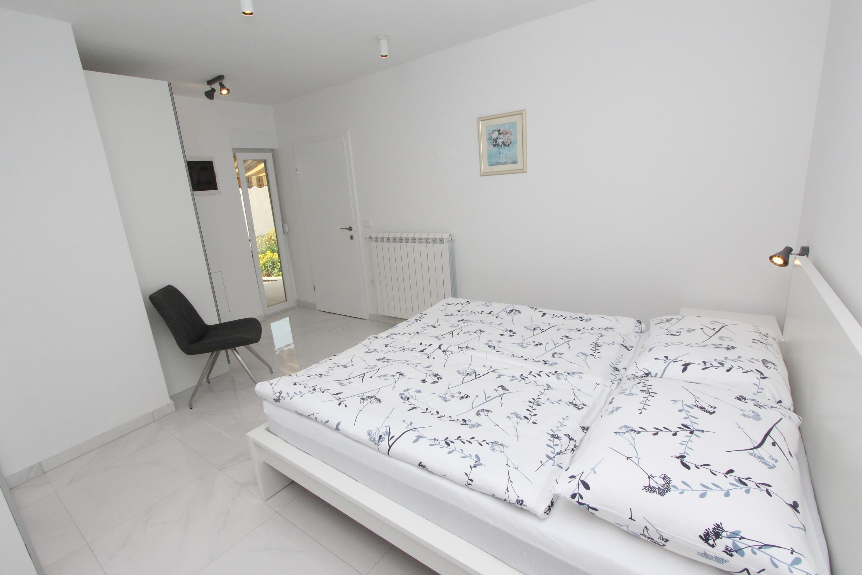 A bedroom with a bed, a chair, a radiator, and a door leading to a balcony.