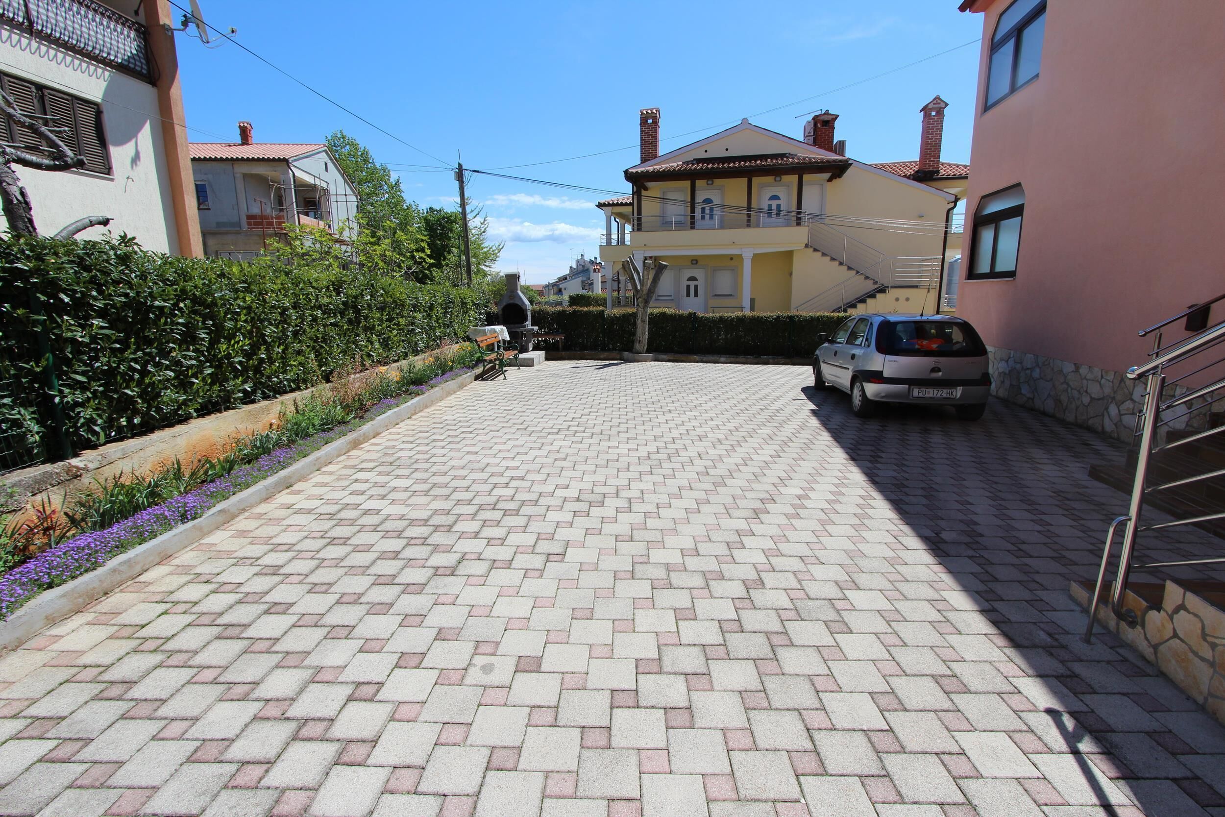 A paved driveway leading to a residential building with a car parked on the side.