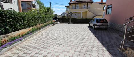A paved driveway leading to a residential building with a car parked on the side.