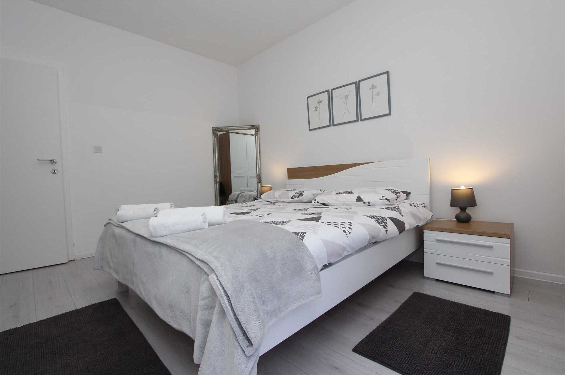 A bedroom with a bed, bedside table, lamp, and a mirror.