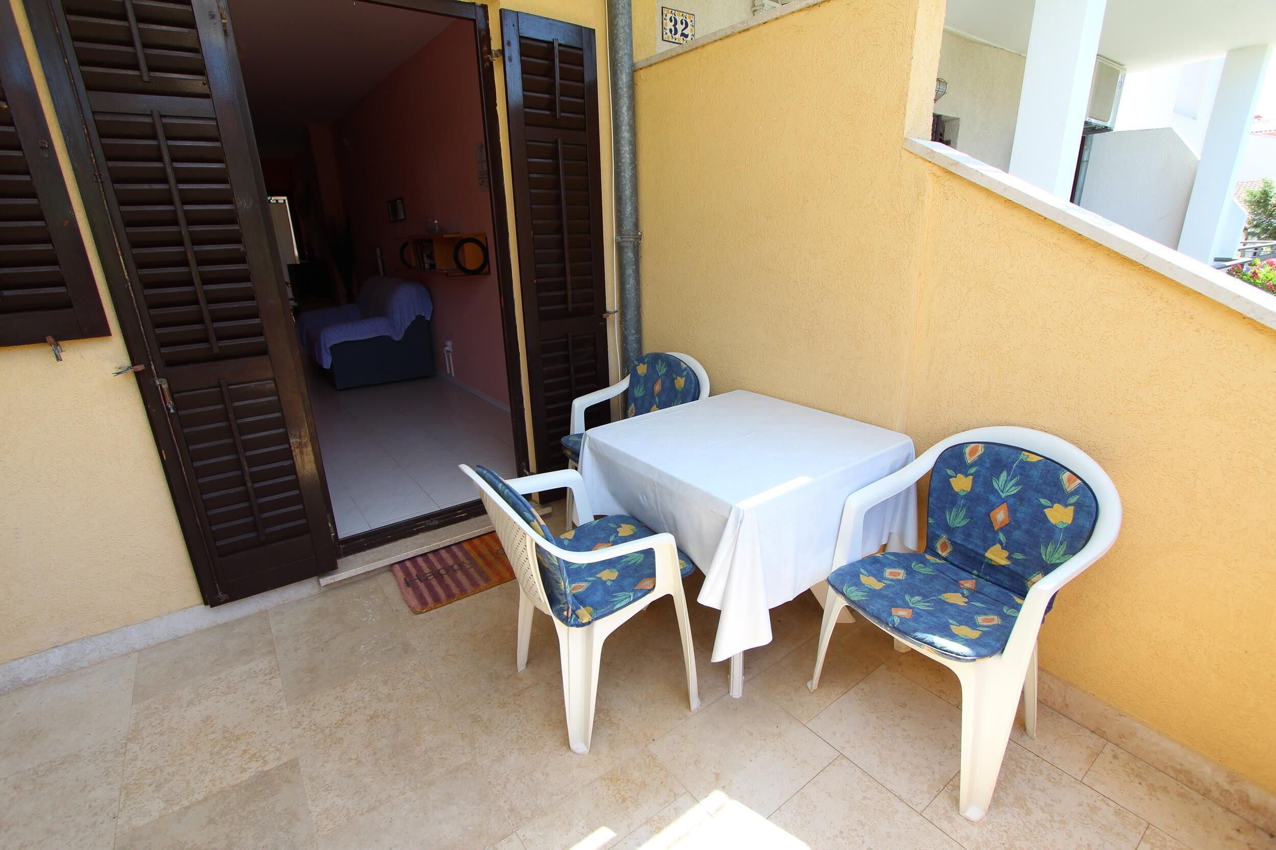A small patio with a table and two chairs, a sliding door, and a window overlooking a building.