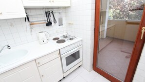 Eine Küche mit weißen Schränken, einem Herd, einem Spülbecken und einem Fenster mit Blick auf einen Balkon.
