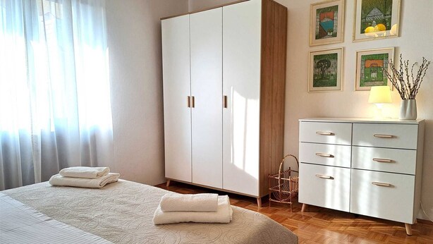 Ein Schlafzimmer mit Bett, Schrank, Kommode und einer Wand mit gerahmten Bildern.