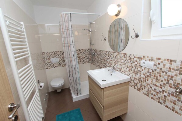 Baño con ducha, inodoro, lavamanos y espejo.