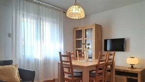 Ein Essbereich mit Holztisch und Stühlen, einem Schrank mit Glastüren, einem Fernseher an der Wand und einer Lampe auf einem Beistelltisch.