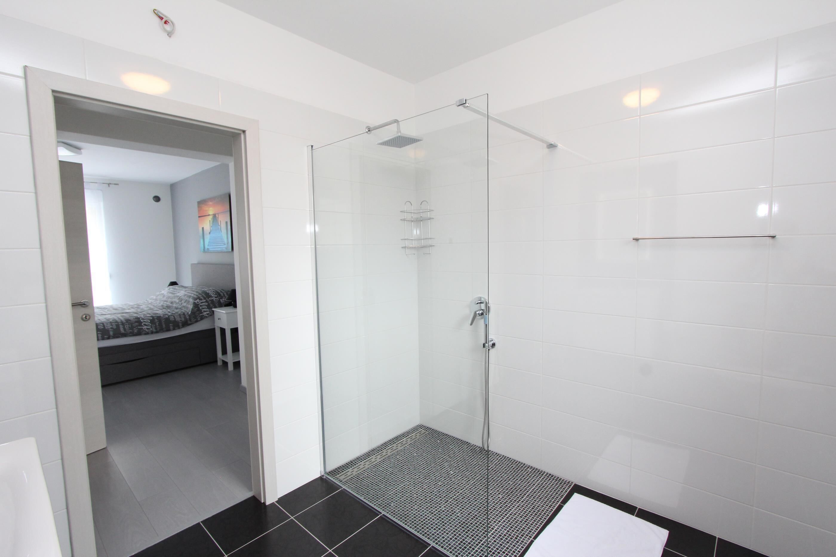 Un bagno moderno con cabina doccia in vetro, pareti piastrellate di bianco e pavimento nero.