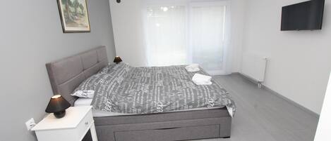 A modern bedroom with a grey bed, white bedside table, and a mounted TV.