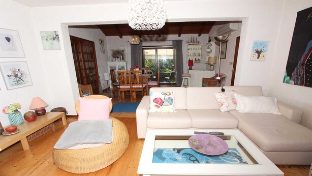 Un salón acogedor con sofá, mesa de centro, reposapiés de mimbre y una zona de comedor al fondo.