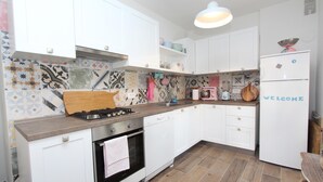 Una cocina con armarios blancos, estufa a gas, lavavajillas y refrigerador.