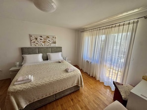 A bedroom with a bed, a nightstand, a bedside table, a window with sheer curtains, and a wall art piece. - ADRI Two-Bedroom Apartment (Rovinj)