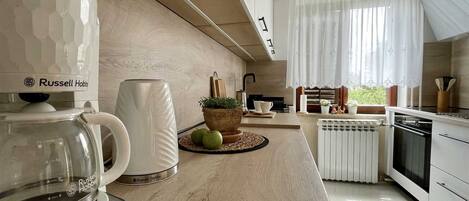 A modern kitchen with a coffee maker, a kettle, and a potted plant on the counter.