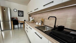 Une cuisine moderne avec un réfrigérateur en acier inoxydable, un plan de travail en bois, un évier et un clavier noir posé sur un plateau.