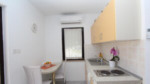 A compact kitchen with a dining area, white walls, a window with a curtain, an air conditioner, a sink, and a small potted plant. - PATAJ One-Bedroom Apartment with Terrace 3 (Rovinj)