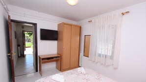 A bedroom with a bed, a wooden wardrobe, a desk, a television, and a window with curtains. - PATAJ One-Bedroom Apartment with Terrace 3 (Rovinj)