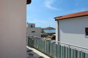 A balcony with a view of a coastal town, a tiled roof, and a metal railing.