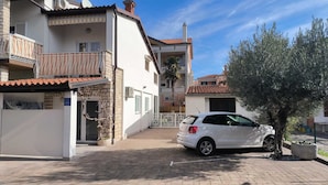 Un edificio residencial con fachada blanca, un balcón con toldo a rayas y un coche blanco estacionado.