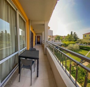 Ein Balkon mit Tisch und Stühlen, Blick auf den Garten, und ein Gebäude im Hintergrund.