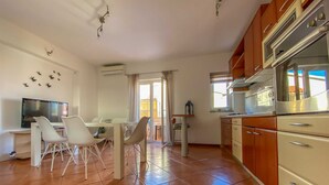 Une cuisine spacieuse dotée d’appareils électroménagers modernes, un coin repas avec des chaises blanches et un téléviseur posé sur un meuble.