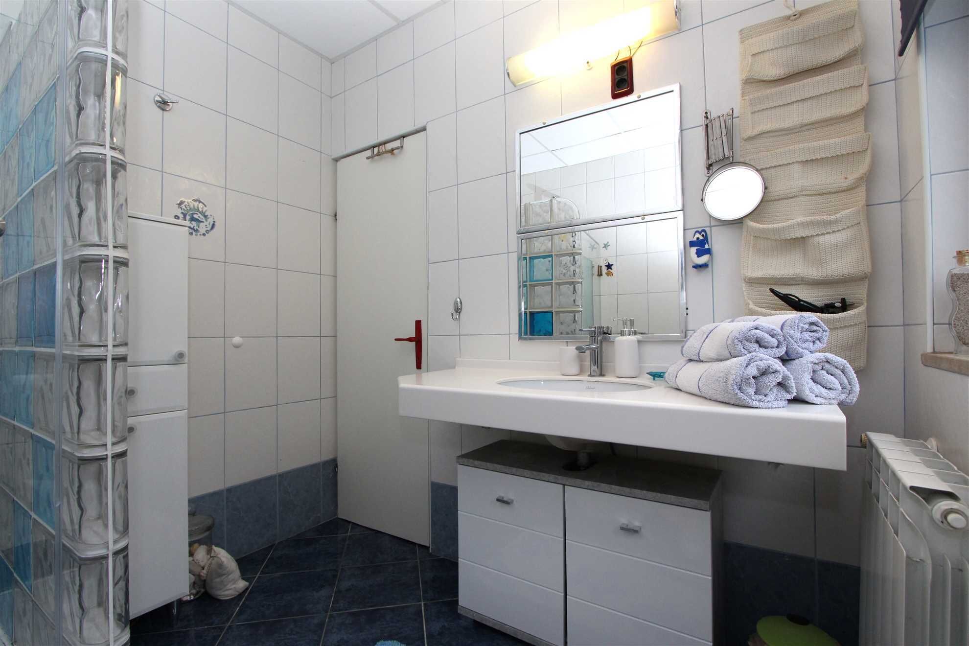 Ein Badezimmer mit einem weißen Waschbecken, Spiegel und Handtuchhalter. Es gibt eine Duschkabine mit Glastür und ebenfalls einen Handtuchhalter.