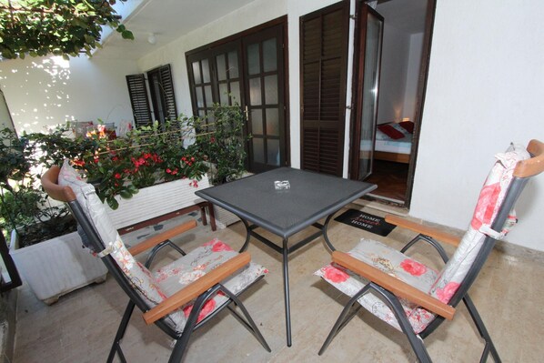 Un patio con una mesa y sillas, una planta en maceta y una puerta corrediza de vidrio que da a un dormitorio.