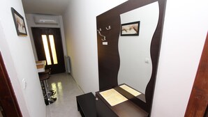 Une pièce comprenant une coiffeuse en bois, un miroir et un banc. On y trouve une porte ornée d’un cadre et un luminaire placé au-dessus.