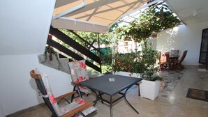 Un patio couvert avec une table et des chaises, une plante en pot et un escalier menant à un niveau supérieur.