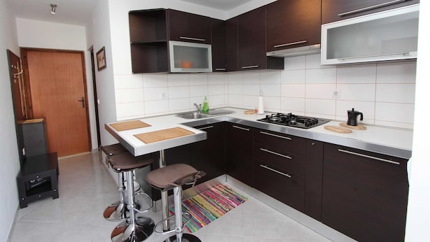 Une cuisine de taille réduite avec des meubles de couleur sombre, un plan de travail blanc, une cuisinière à gaz et deux tabourets de bar.