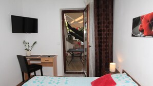 Une chambre à coucher comprenant un lit, un bureau, une chaise, un téléviseur et une porte donnant sur un balcon.