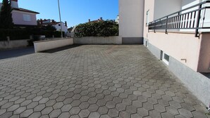 A paved outdoor area with a hexagonal tile pattern, a white building with a balcony, and a hedge in the background. - ELIDA Studio Apartment (Rovinj)