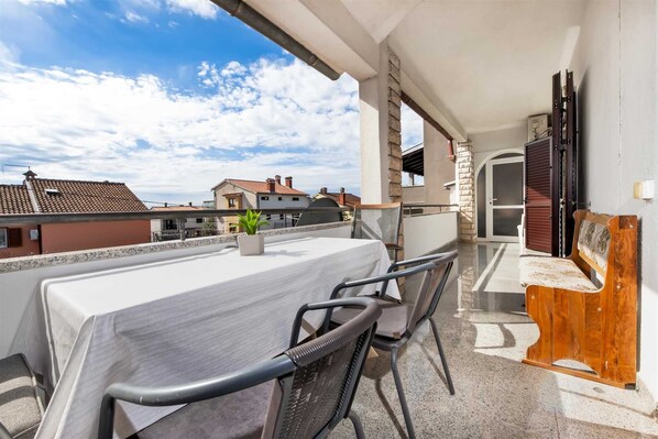 A balcony with a table and chairs, a potted plant, and a wooden bench.
