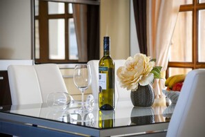 A table with a bottle of wine, a vase with flowers, and a fruit bowl.