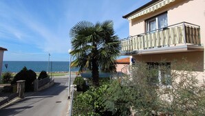A residential building with a balcony, a palm tree, and a view of the sea.
