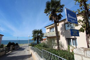 Un bâtiment situé sur la côte, avec une enseigne indiquant « SOBE - CAMER - ZIMMER - CHAMBRES - APPARTEMENTS » et « SLOBODNO LIBERO FREI / LIBRE ».