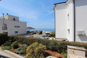 Un edificio frente al mar, con vistas al océano, zona de estacionamiento y un jardín lleno de flores amarillas.