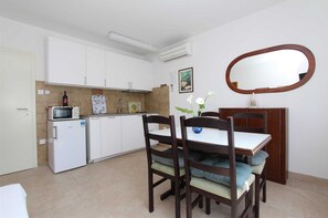 Cocina compacta con gabinetes blancos, microondas, refrigerador y comedor con mesa y sillas.