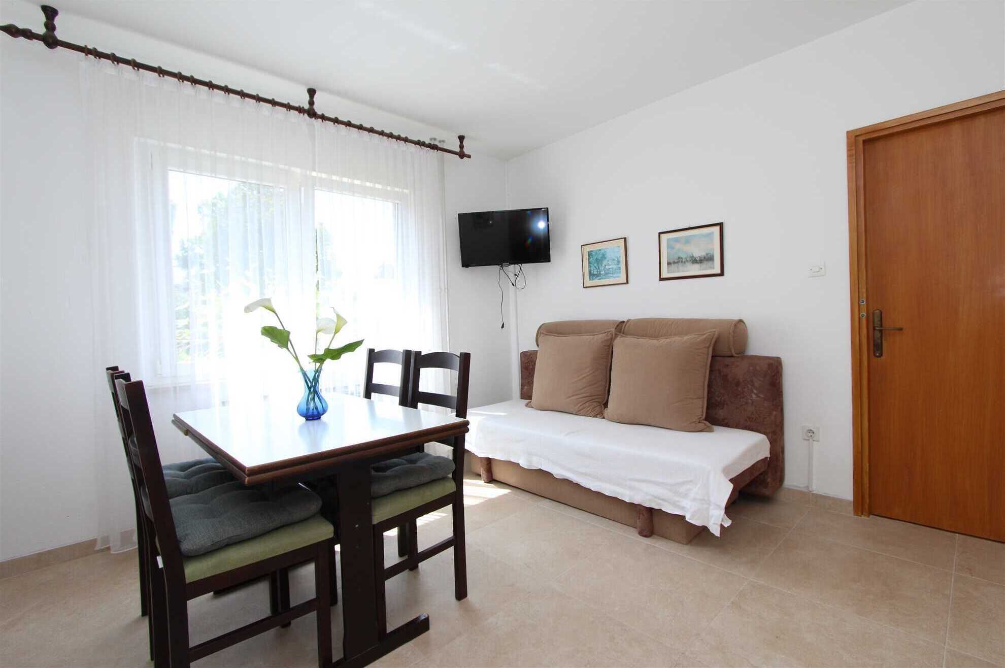 Een kamer met een eettafel, stoelen, een bank, een televisie en een deur.