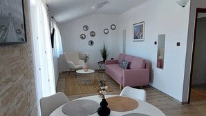 A modern living room with a white sofa, a dining table with white chairs, and a kitchen area in the background. - MATOSEVIC One-Bedroom Apartment with Balcony 1 (Rovinj)