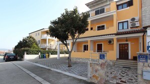 A yellow building with a stone entrance, a tree in front, and a car parked on the street. - MATOSEVIC One-Bedroom Apartment with Balcony 1 (Rovinj)