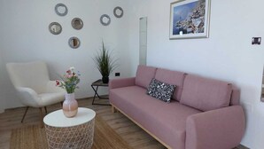 A living room with a white armchair, a pink sofa, a round coffee table, and a potted plant. - MATOSEVIC One-Bedroom Apartment with Balcony 1 (Rovinj)