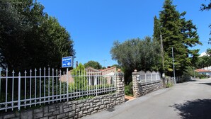 Un lotissement résidentiel fermé, délimité par un mur de pierre et une clôture en métal, avec un panneau bleu indiquant un immeuble d’appartements, et des maisons en arrière-plan.