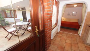 Une pièce avec un mur en briques, un lit recouvert d’une couverture rouge et une fenêtre avec un rideau.