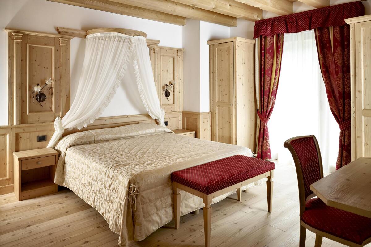 Een slaapkamer met een houten bed, een nachtkastje, een bankje, een stoel en een kledingkast.