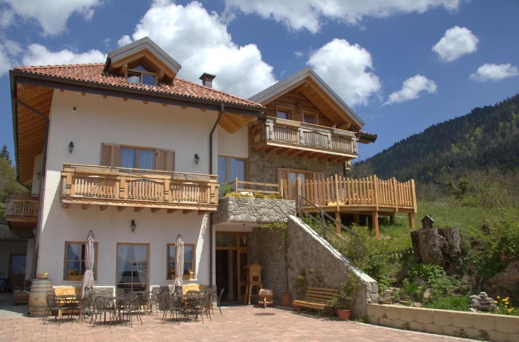 Un chalet a due piani con facciata in pietra, balconi in legno e una zona patio con posti a sedere esterni.