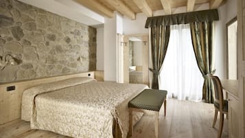 Camera da letto con parete in pietra, travi in legno a vista al soffitto, un letto con copripiumino decorato, una panca e tende.
