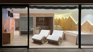 Une salle de spa moderne avec un lambris en bois, deux fauteuils, une table de massage et une cabine de douche en verre.