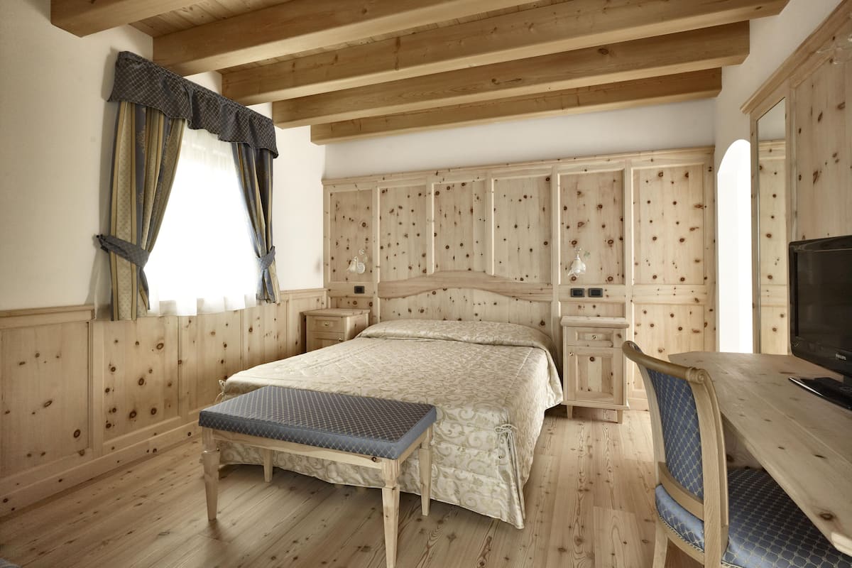 Een slaapkamer met houten lambrisering, een bed, nachtkastjes, een bureau en een stoel.