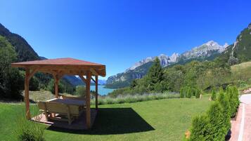 A wooden gazebo with a bench, surrounded by a well-maintained lawn and a view of mountains and a lake.